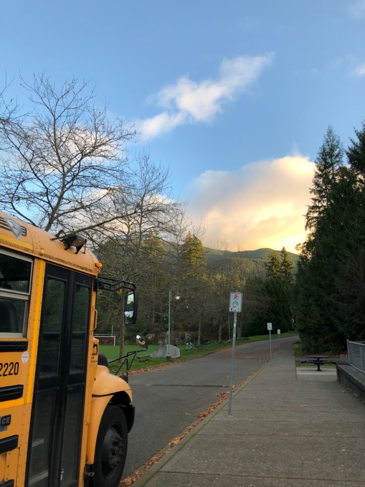 a yellow school bus parked on the side of a road next to a park bench