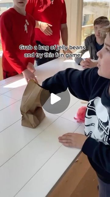 a young boy holding a paper bag while standing next to two other boys at a table