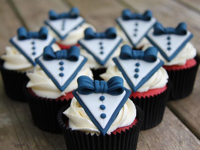 cupcakes decorated with bow ties and tuxedos are sitting on a wooden table