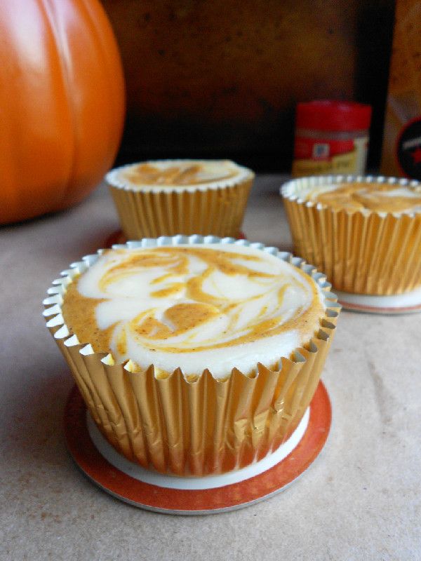 three cupcakes with white frosting sitting on top of a table next to a pumpkin