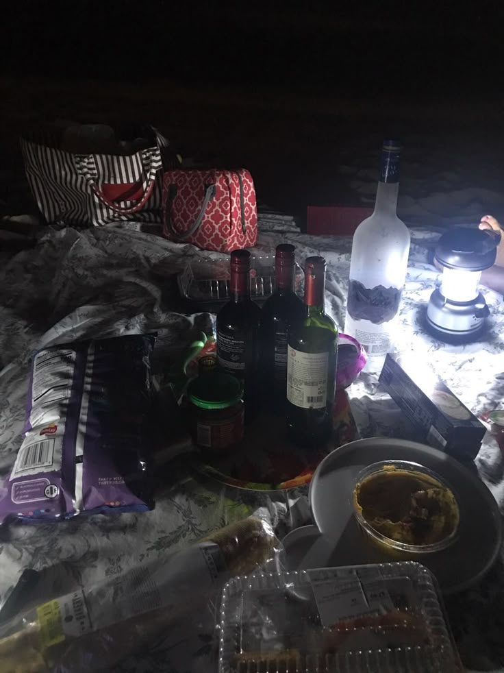 a table topped with lots of food and drinks next to a bottle of wine on top of a bed