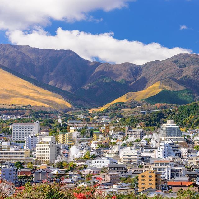 a city with mountains in the background and clouds in the sky over it, surrounded by trees