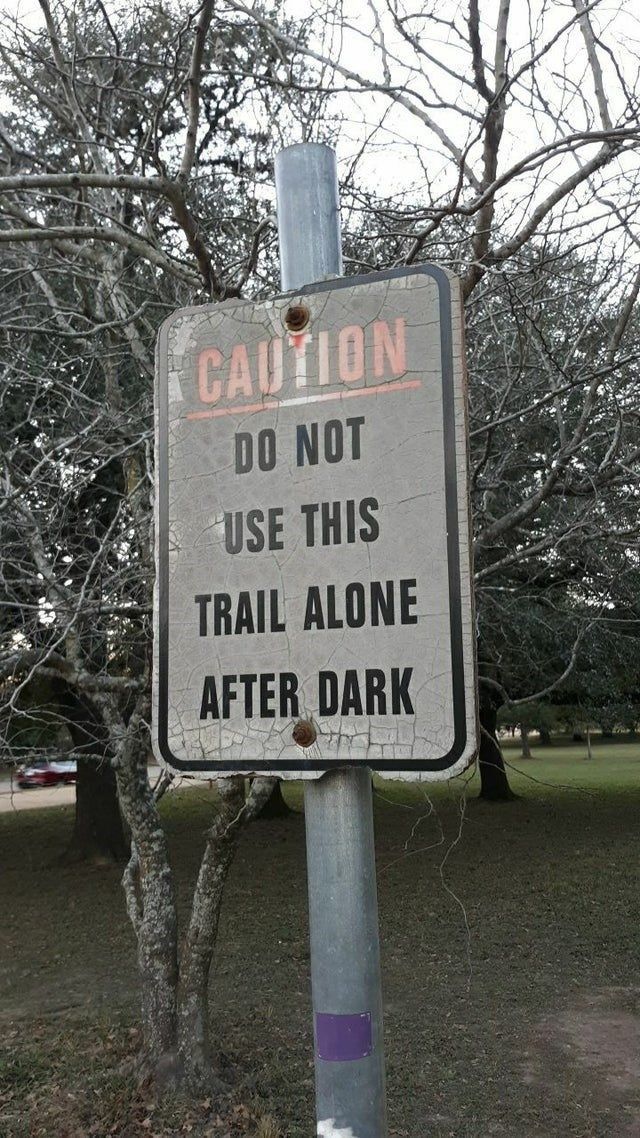 a caution sign posted on a metal pole in front of a tree with no leaves