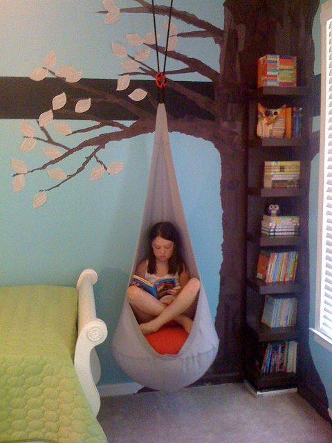 a woman sitting in a hammock reading a book next to a bookshelf