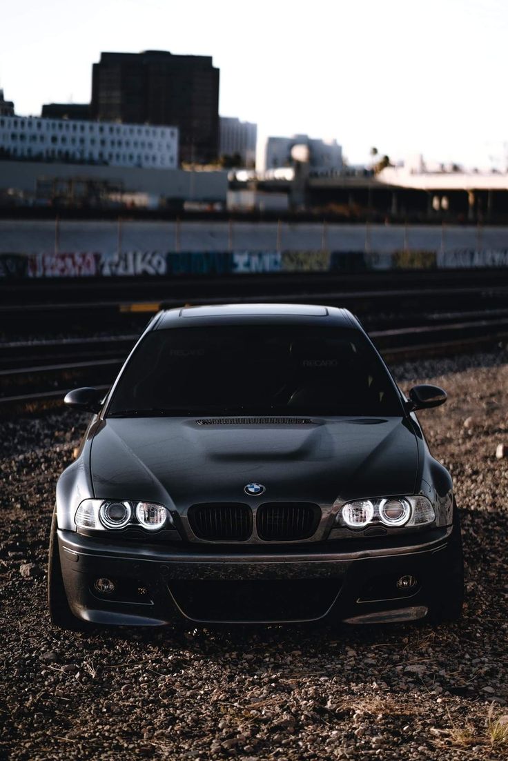 a black car parked on the side of train tracks in front of a city skyline