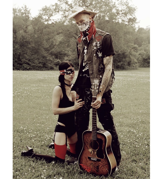 a man and woman standing next to each other in the grass with a guitar behind them