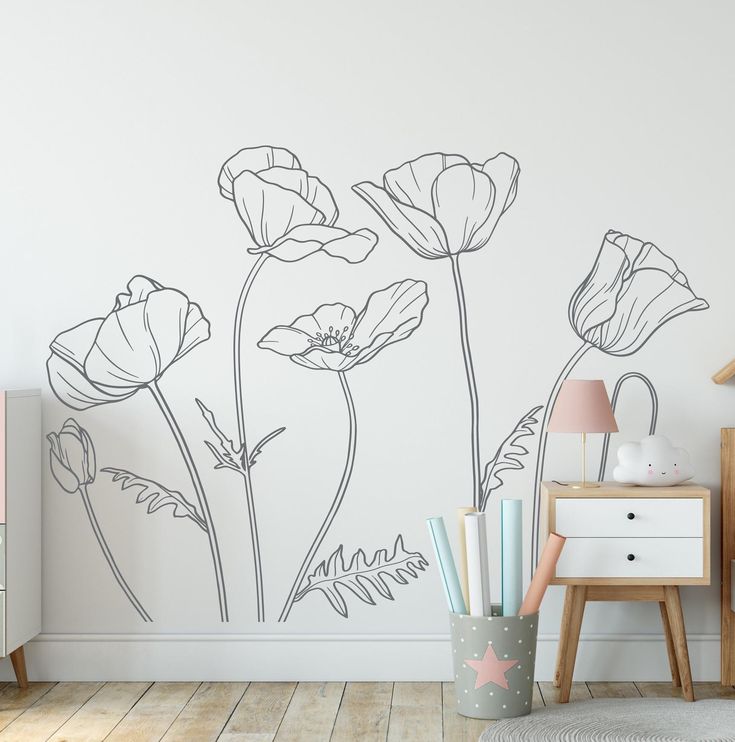 a white wall with flowers painted on it and a lamp next to the dresser in front