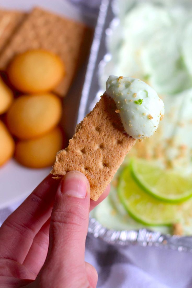 a person holding up a cracker with ice cream and limes in the background