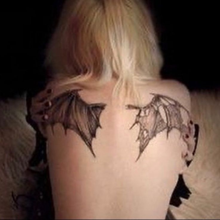 the back of a woman's body with tattoos on her shoulder and wings drawn in black ink