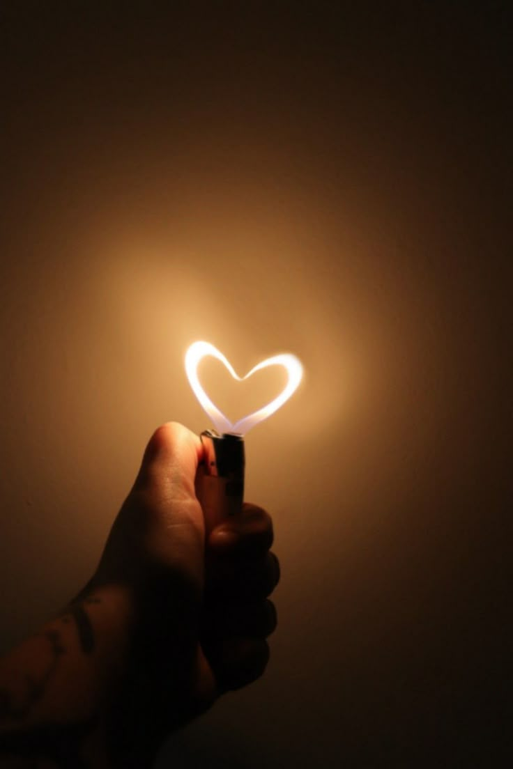 a hand holding a lighter with a heart shaped light on it's side in the dark