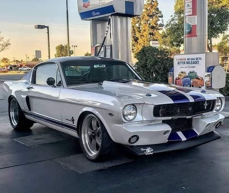 an old ford mustang is parked at a gas station in front of a fuel pump