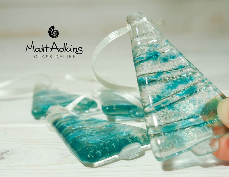 a hand holding a glass christmas tree ornament on top of a white table