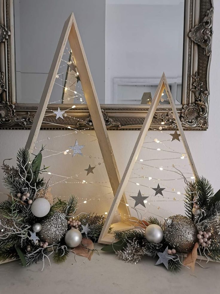 two christmas trees with lights and ornaments in front of a mirror on a mantle or mantel