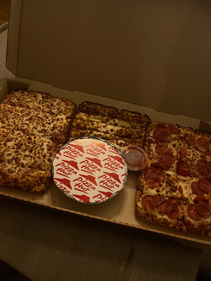 several different types of pizzas in a box on a table with one slice missing