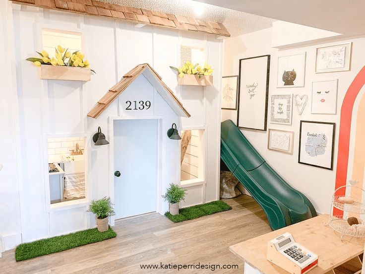 a dog house with a green slide in the corner and pictures on the wall behind it