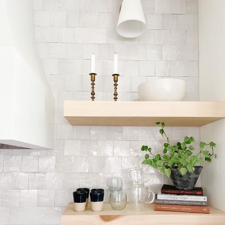 a shelf with some plants and glasses on it in a room that has white brick walls