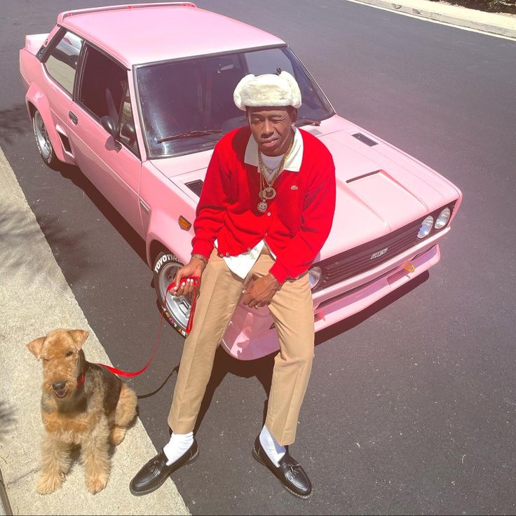 a man sitting on the hood of a pink car next to a brown and white dog