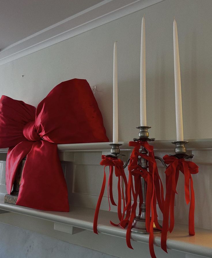 a red bow is tied around candles on a mantle