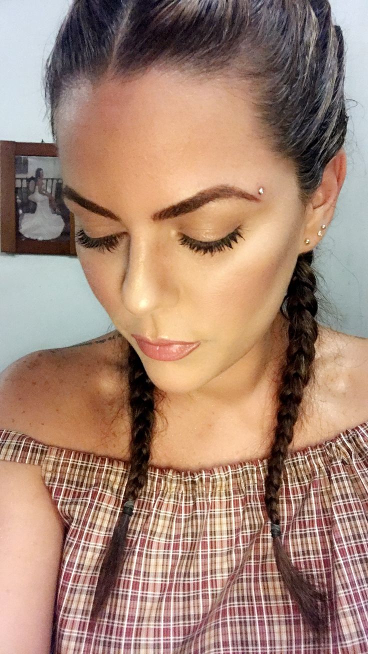 a woman with braids and makeup looks down at her cell phone while wearing an off the shoulder top