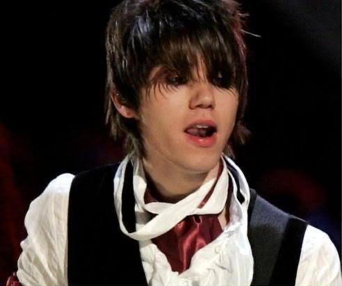 a young man wearing a vest and tie with his mouth open while singing into a microphone