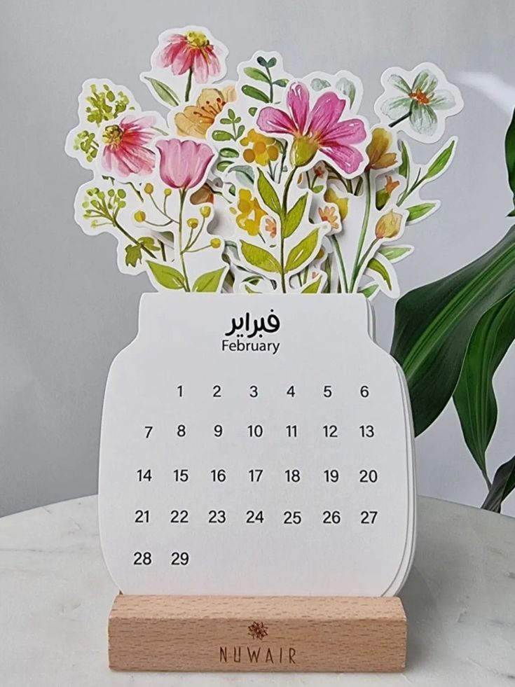 a calendar with flowers on it sitting next to a plant