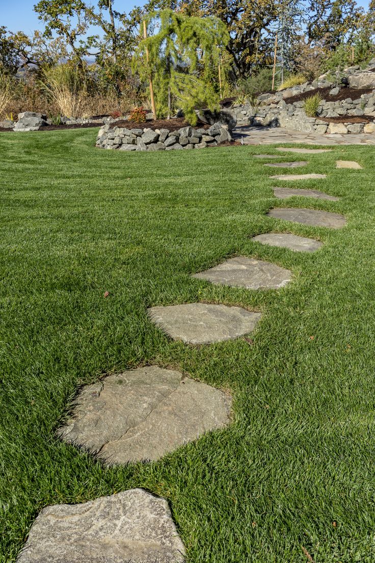 a stone path in the grass leading to some trees