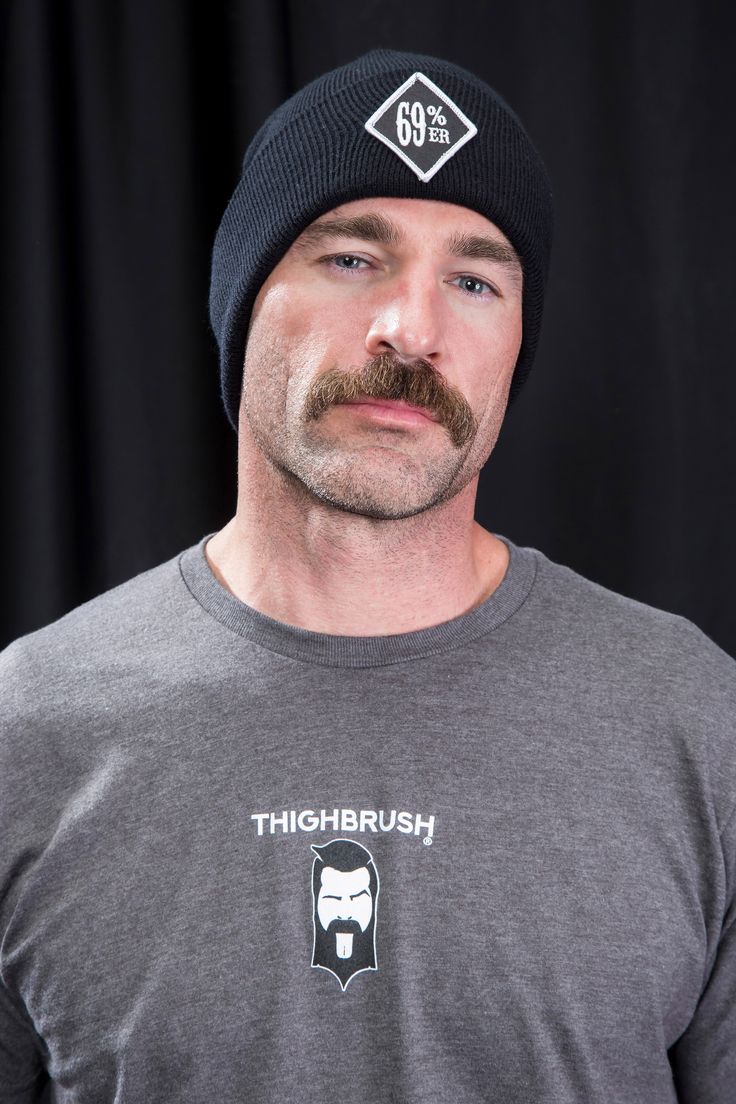 a man with a beard wearing a black hat and grey t - shirt is looking at the camera