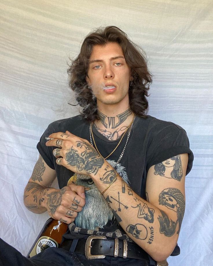 a man with long hair and tattoos holding a bottle