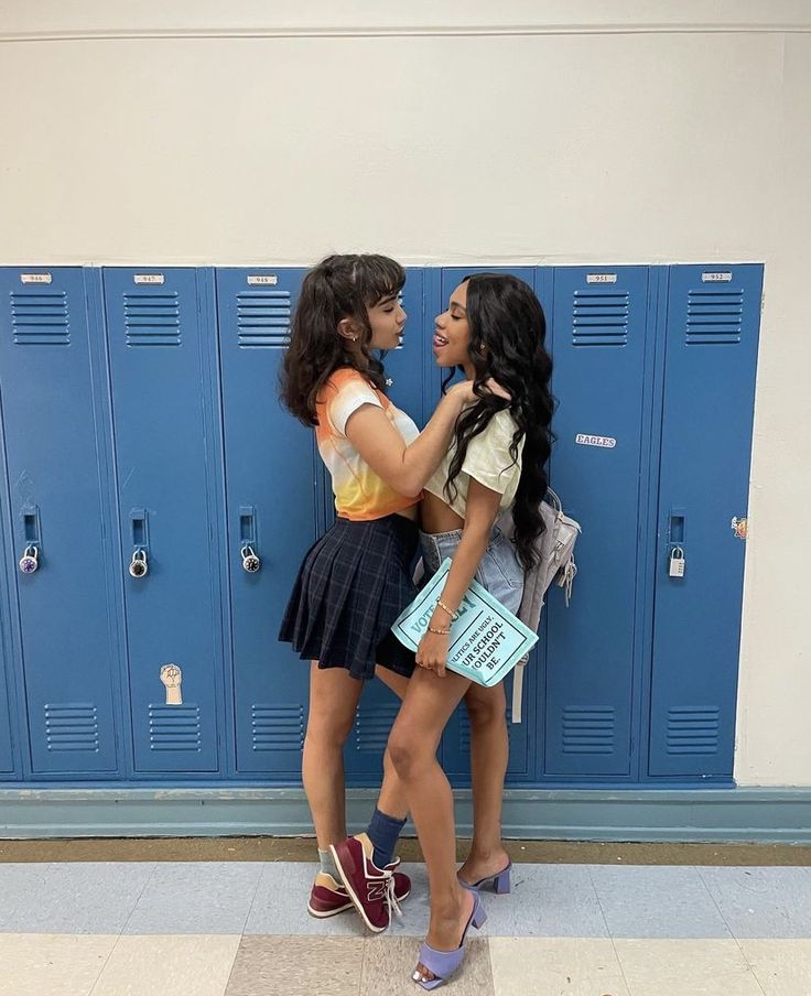 two young women standing next to each other in front of blue lockers with their backs turned