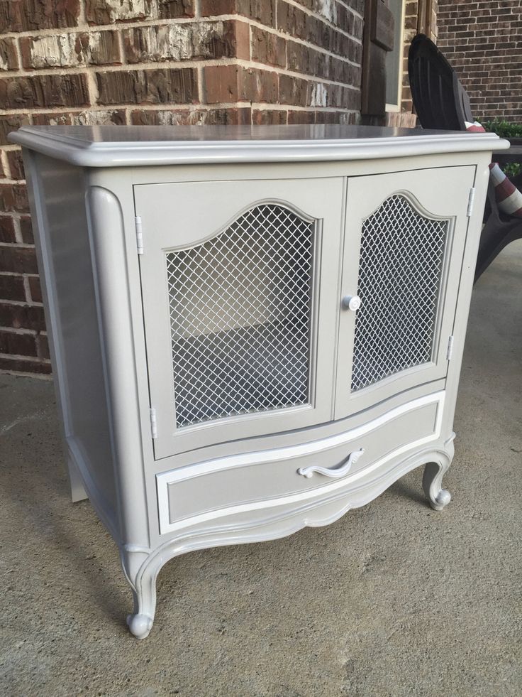 a white cabinet with glass doors on the top and bottom, sitting in front of a brick wall