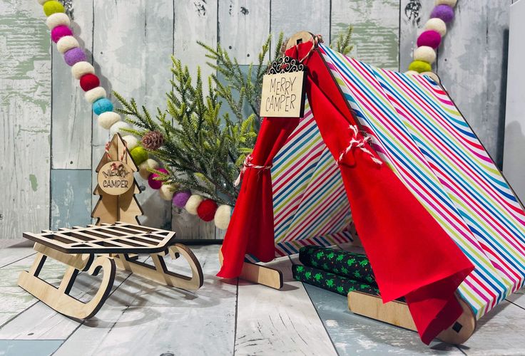 a small wooden sleigh next to a christmas tree with presents wrapped around it