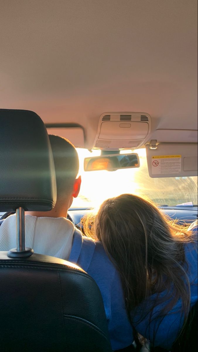 two people sitting in the back seat of a car with sun shining down on them