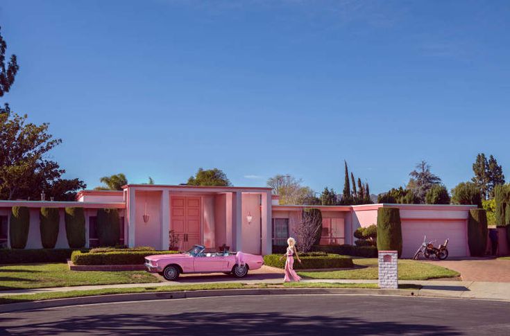 a pink car is parked in front of a house with hedges and bushes on either side