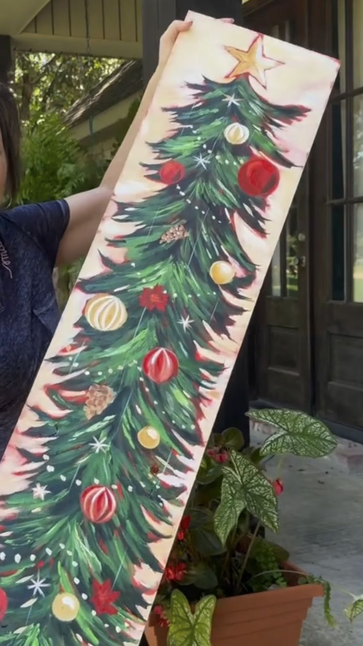 a woman holding up a christmas tree painting