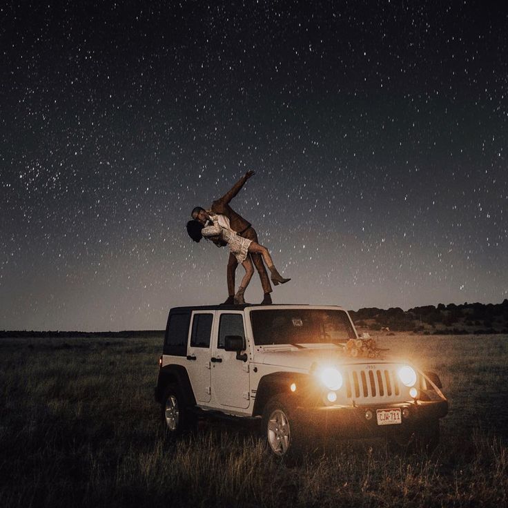 two people standing on top of a jeep in the middle of a field at night