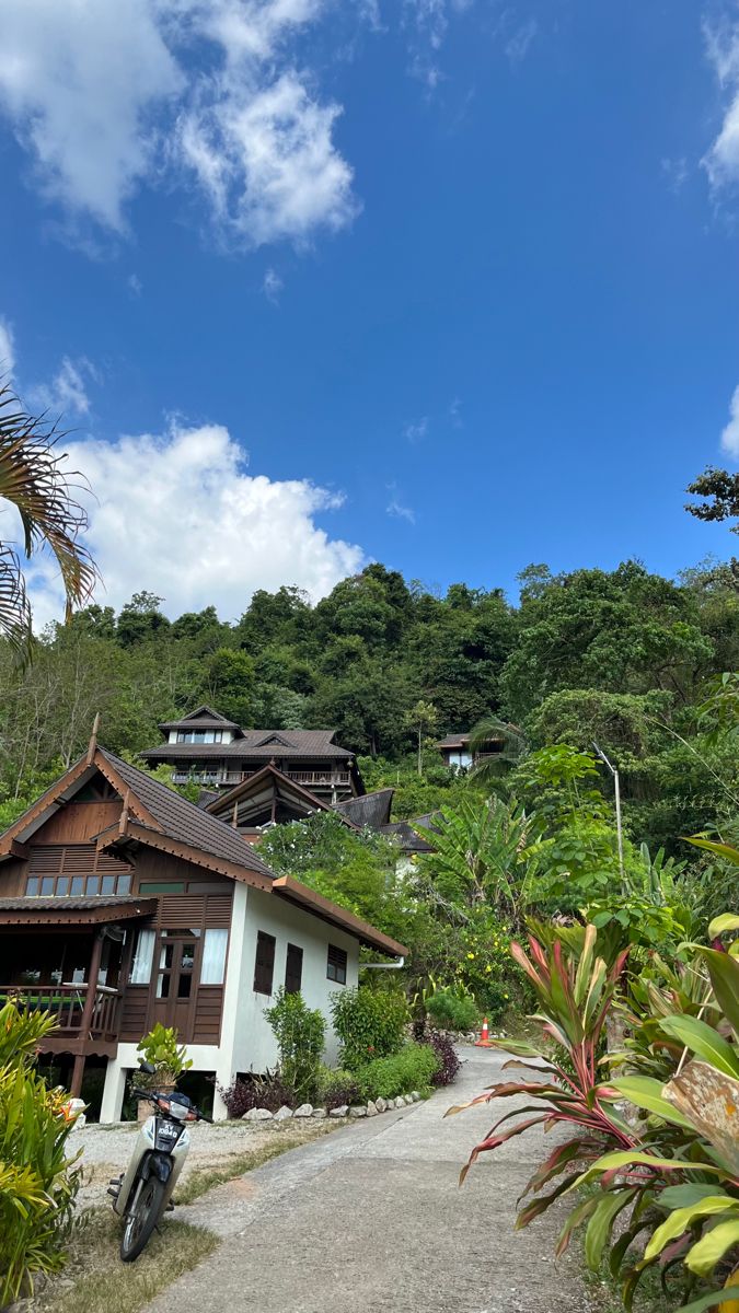 a motorcycle parked in front of a house on the side of a hill with palm trees