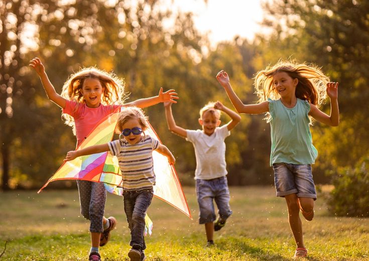 four children running in the grass with kites