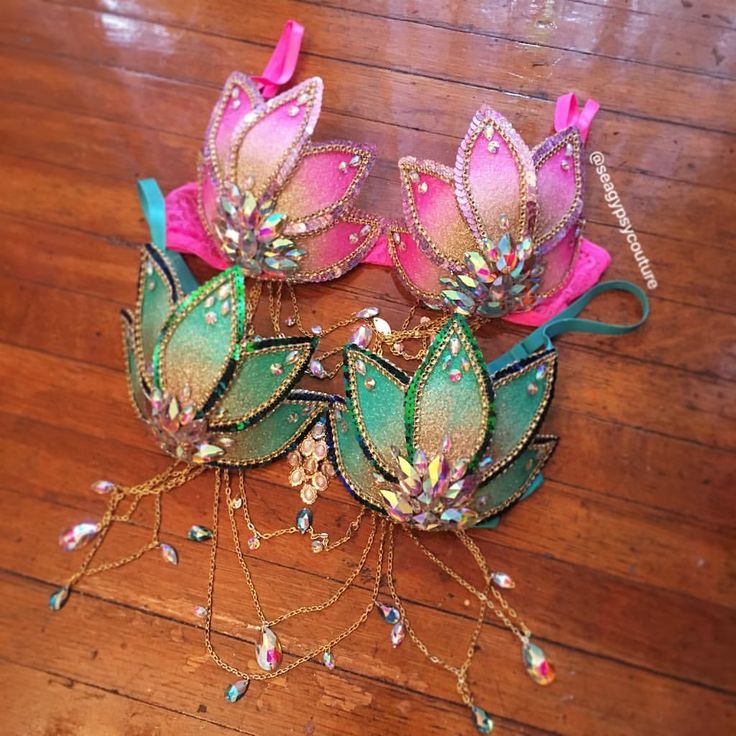 two pink and green flowers with chains attached to them on a wooden floor next to a pair of hair clips