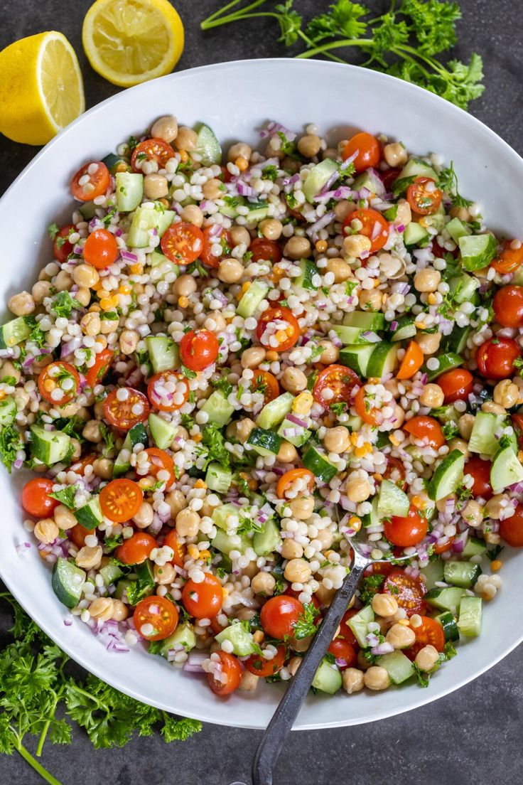 a white bowl filled with salad and garnished with tomatoes, cucumbers, chickpeas, and other vegetables