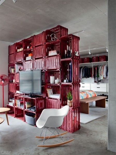 a living room filled with lots of red crates and shelves next to a white rocking chair