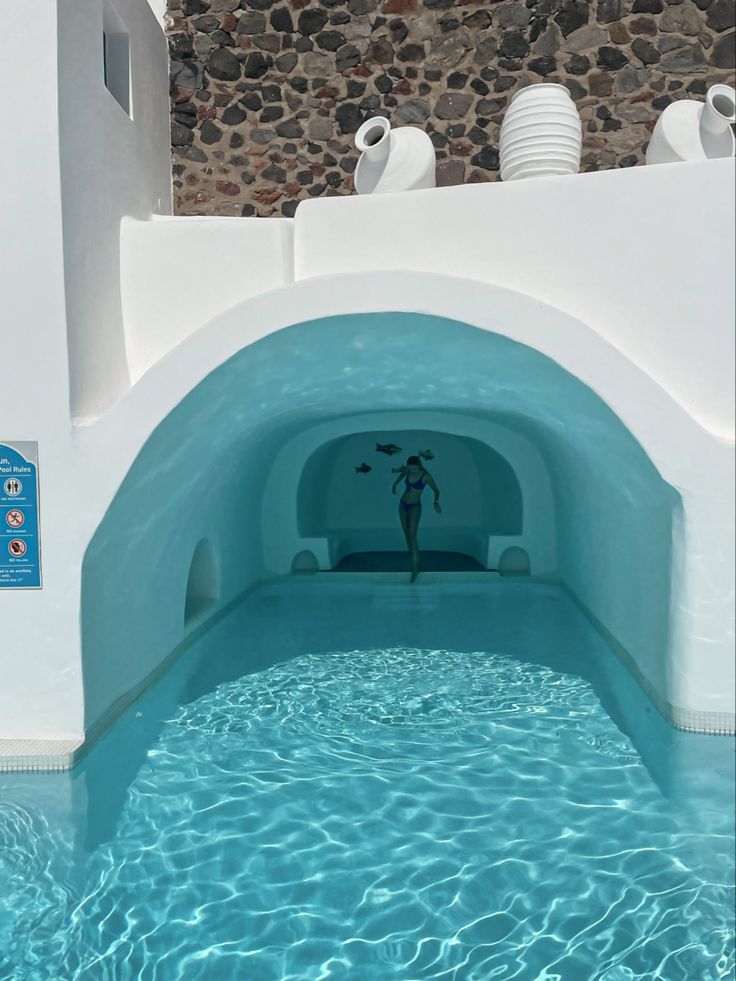 an indoor swimming pool with blue water and white walls is pictured in this image, it appears to have been built into the side of a stone wall