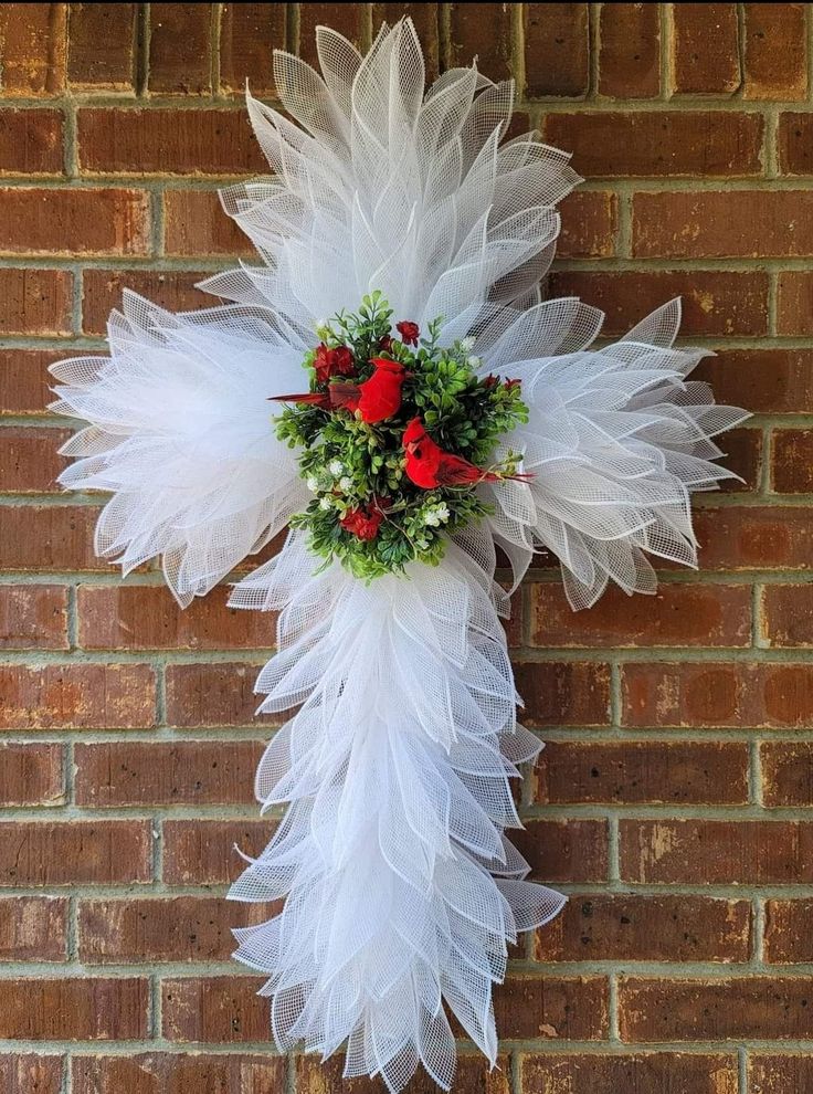 a cross made out of white tulle with red roses and greenery on it