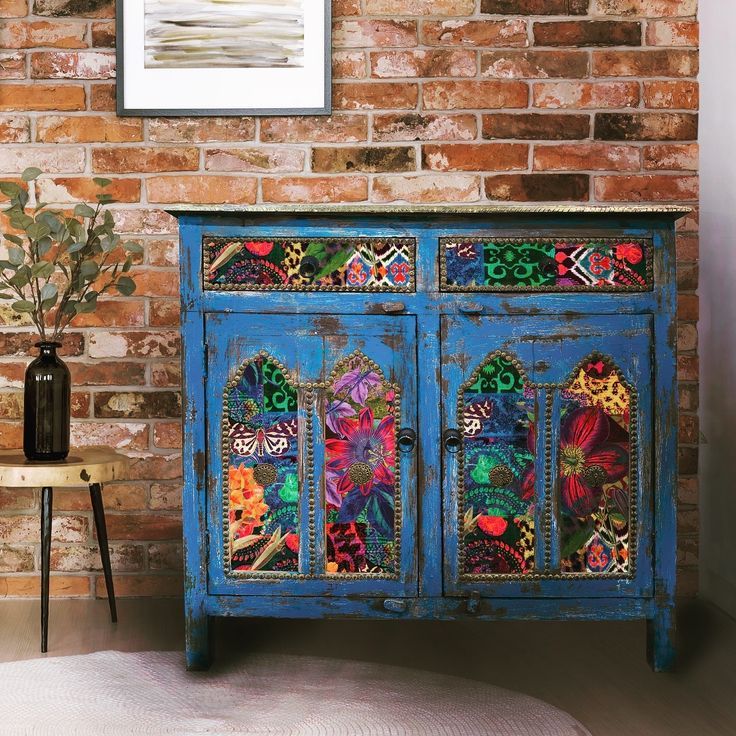 a blue painted cabinet with colorful designs on the doors and drawers in front of a brick wall