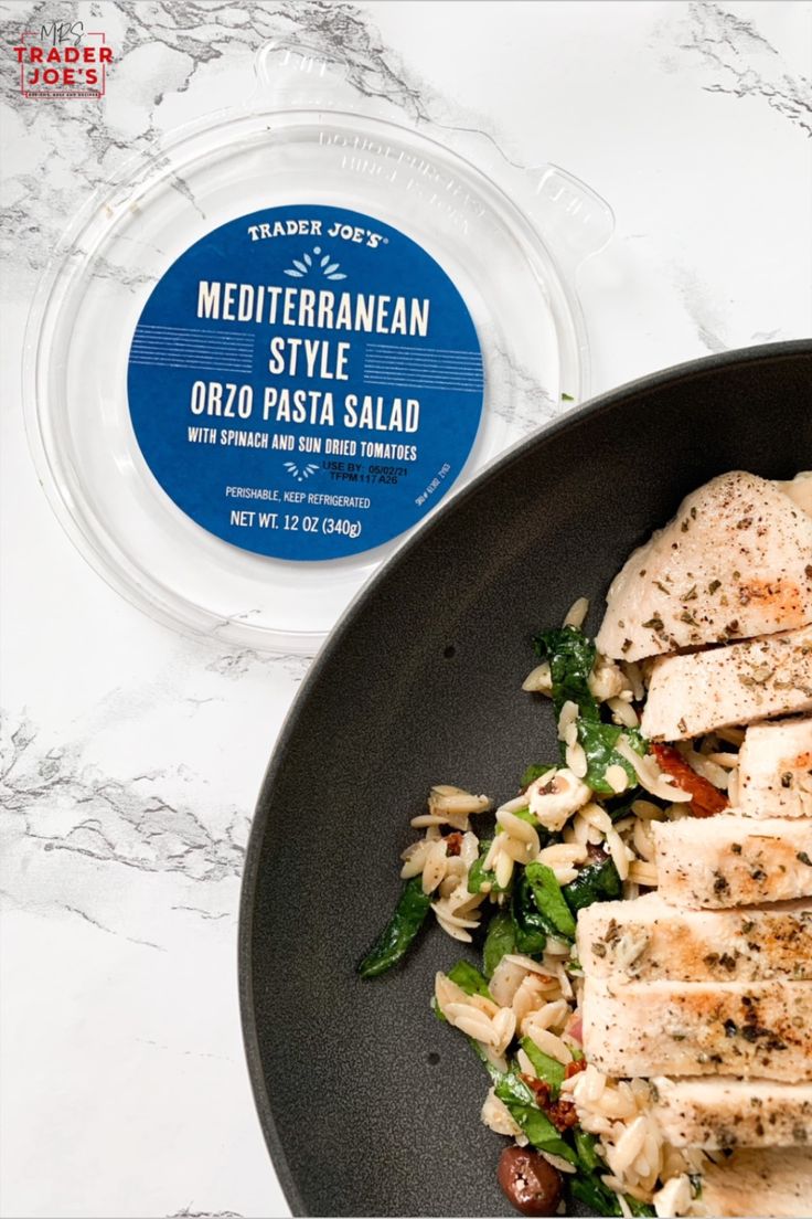 a pan filled with chicken and pasta next to a container of mediterranean style dressing