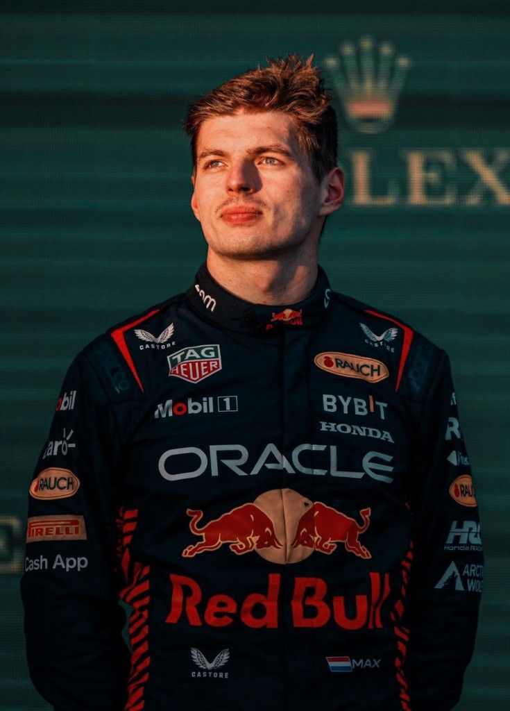 a man standing in front of a green wall wearing a red bull uniform and looking off to the side