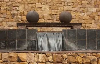 a stone building with three balls on the roof and water running down it's side