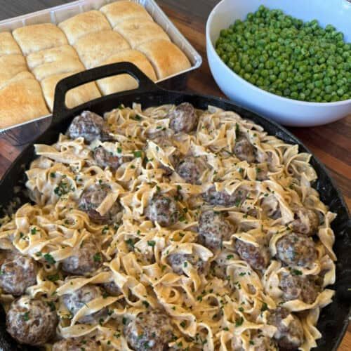 a pan filled with pasta and meatballs next to peas