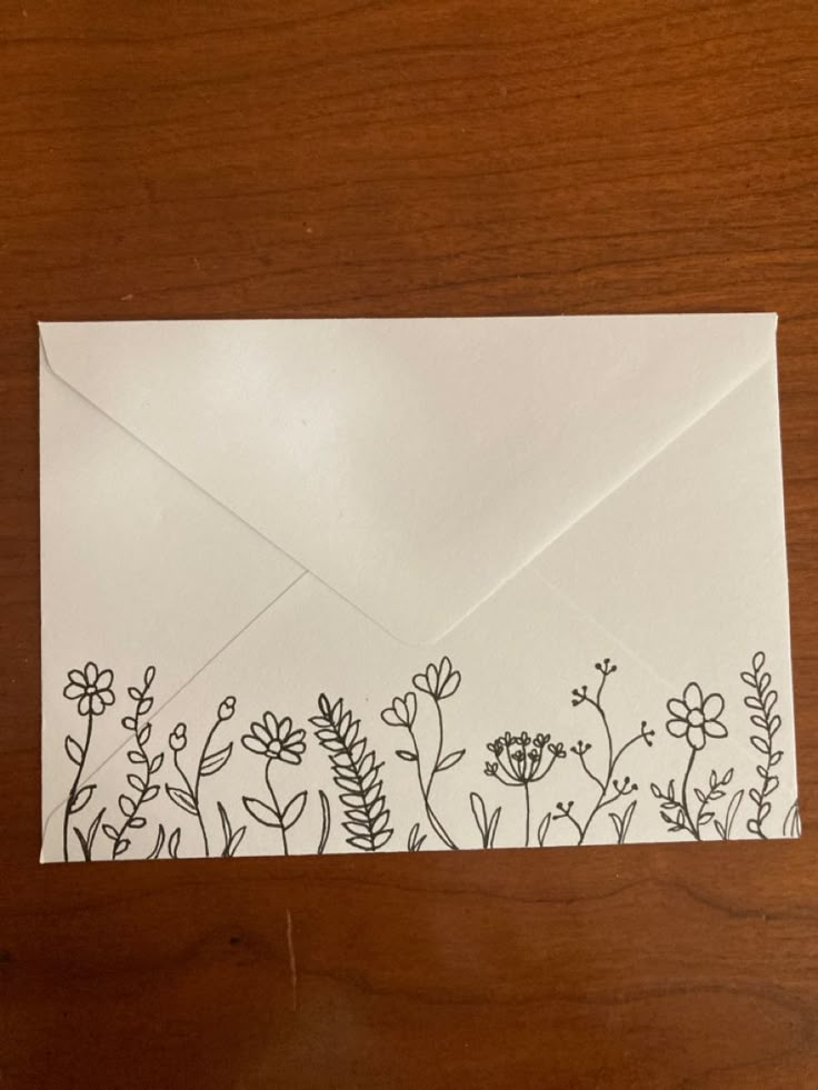 an envelope with flowers drawn on it sitting on top of a wooden table next to a piece of paper