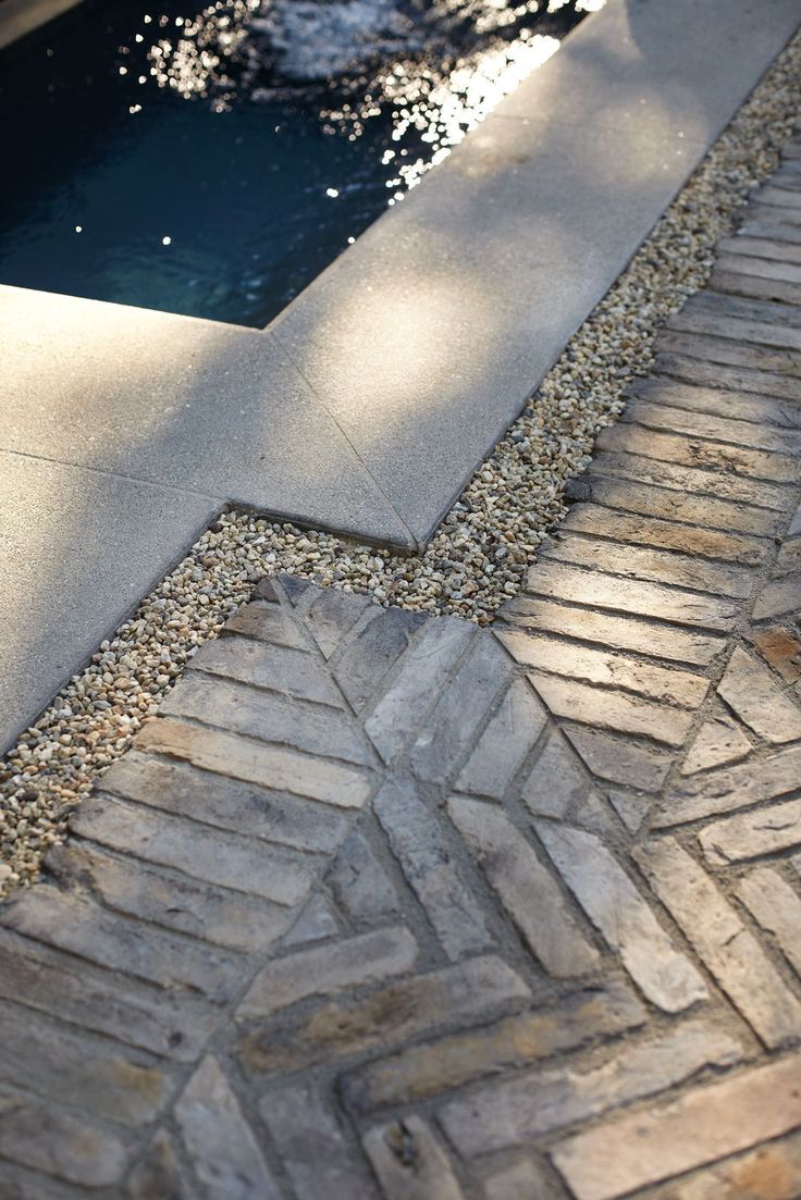 a brick walkway next to a pool with water in it