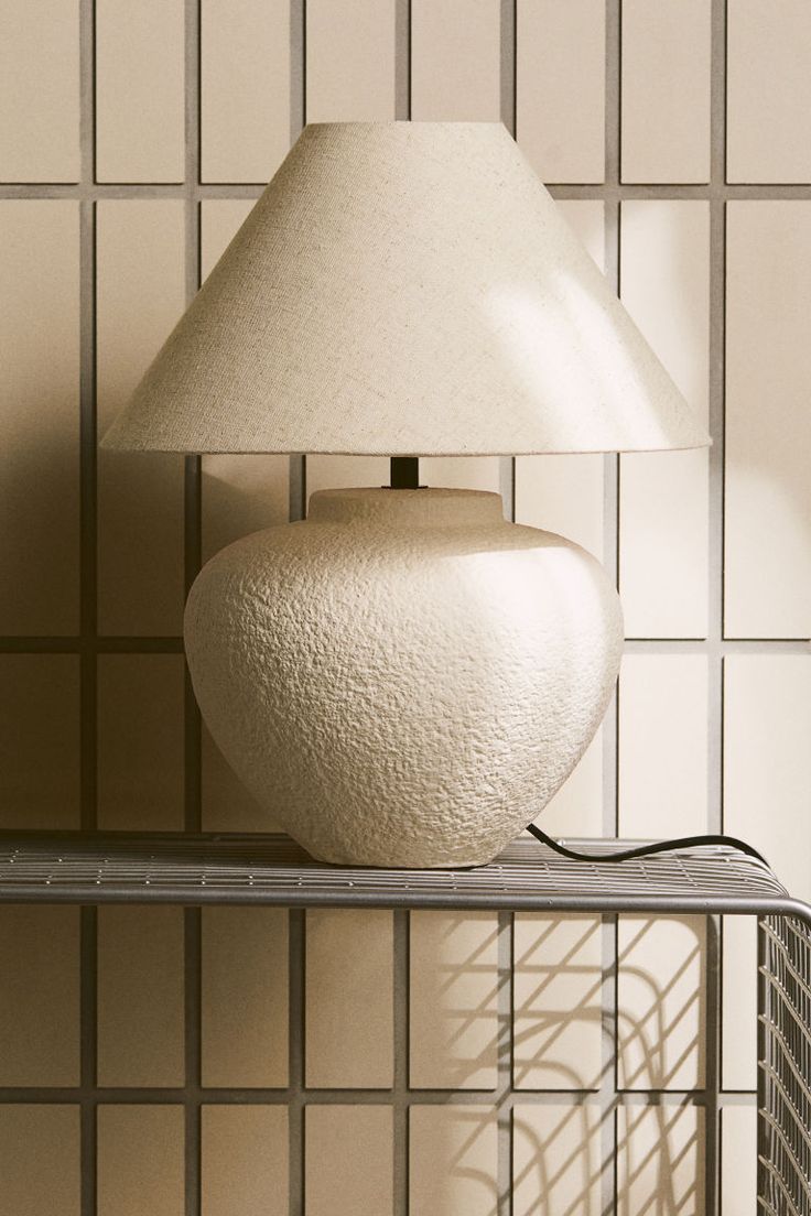 a white lamp sitting on top of a shelf next to a wall covered in tiles